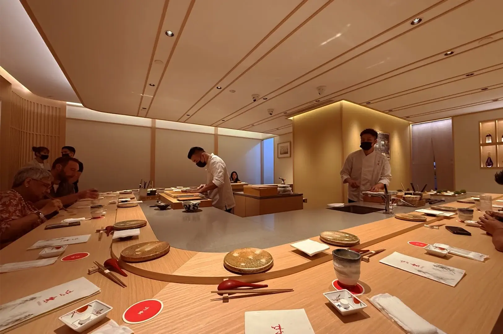 Inside Miraku at Icon Village, a minimalist, upscale Japanese restaurant in Tanjong Pagar featuring a curved wooden sushi counter where chefs prepare omakase for diners.