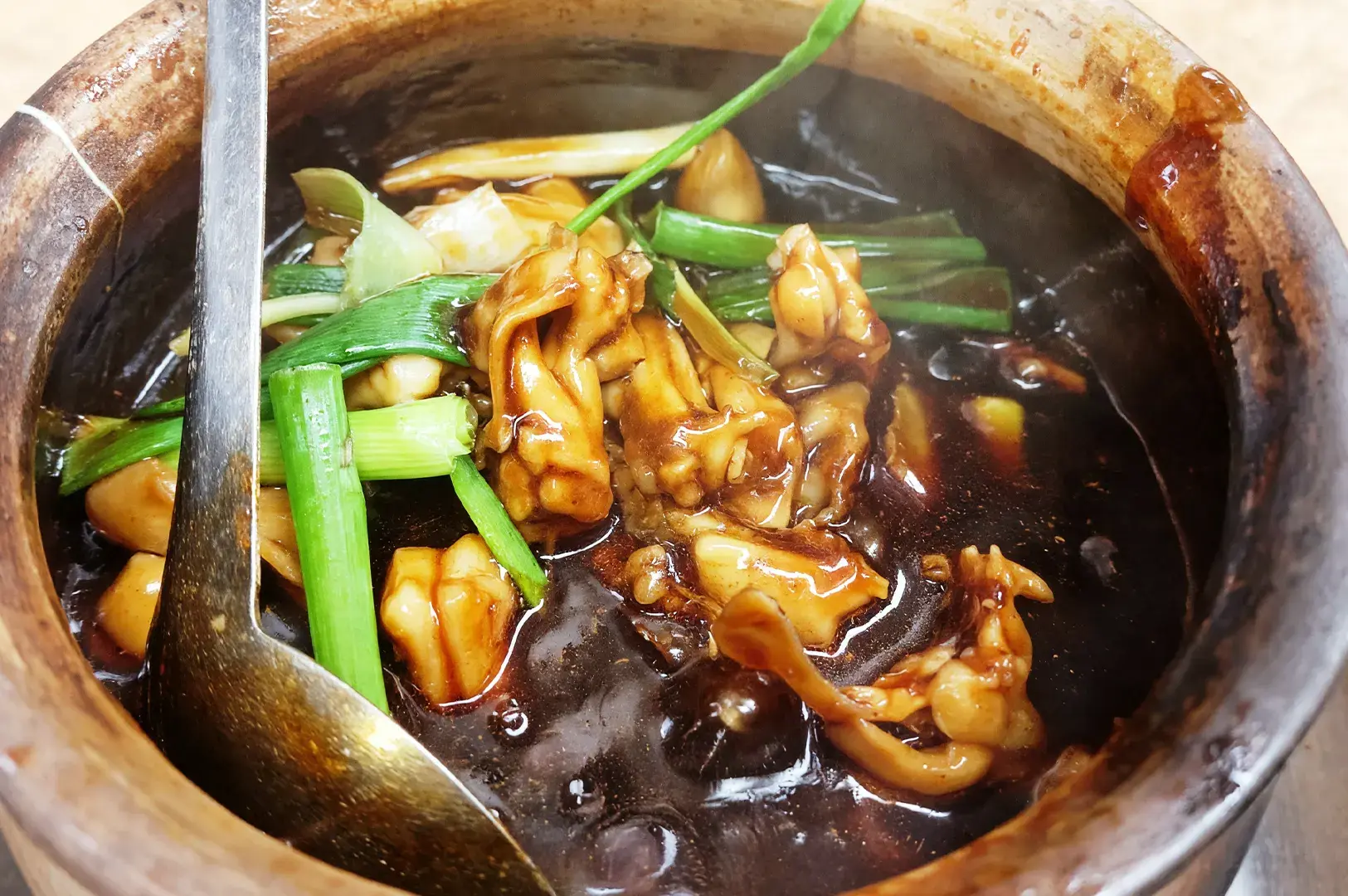 A steaming claypot of frog legs cooked in a savory dark sauce with fresh spring onions, a classic dish that highlights Geylang’s popular late-night supper traditions.