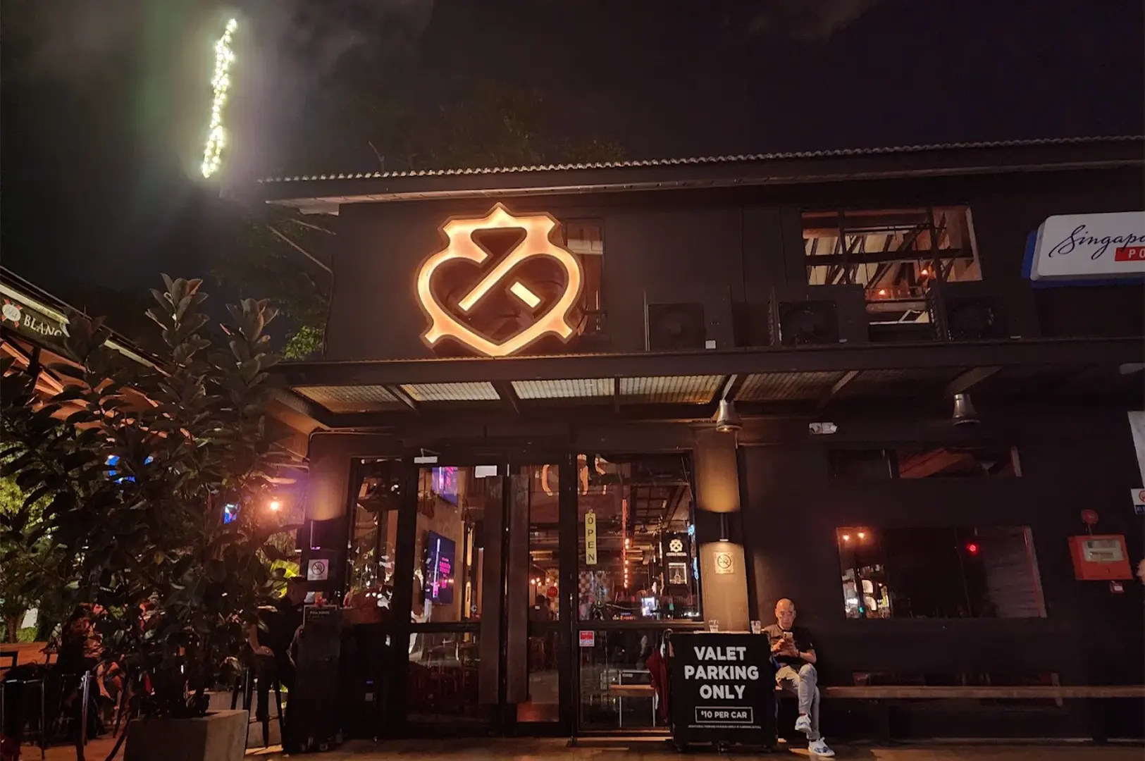 The illuminated exterior facade of KPO Café Bar in Singapore at night, featuring its signature logo, dark industrial aesthetic.