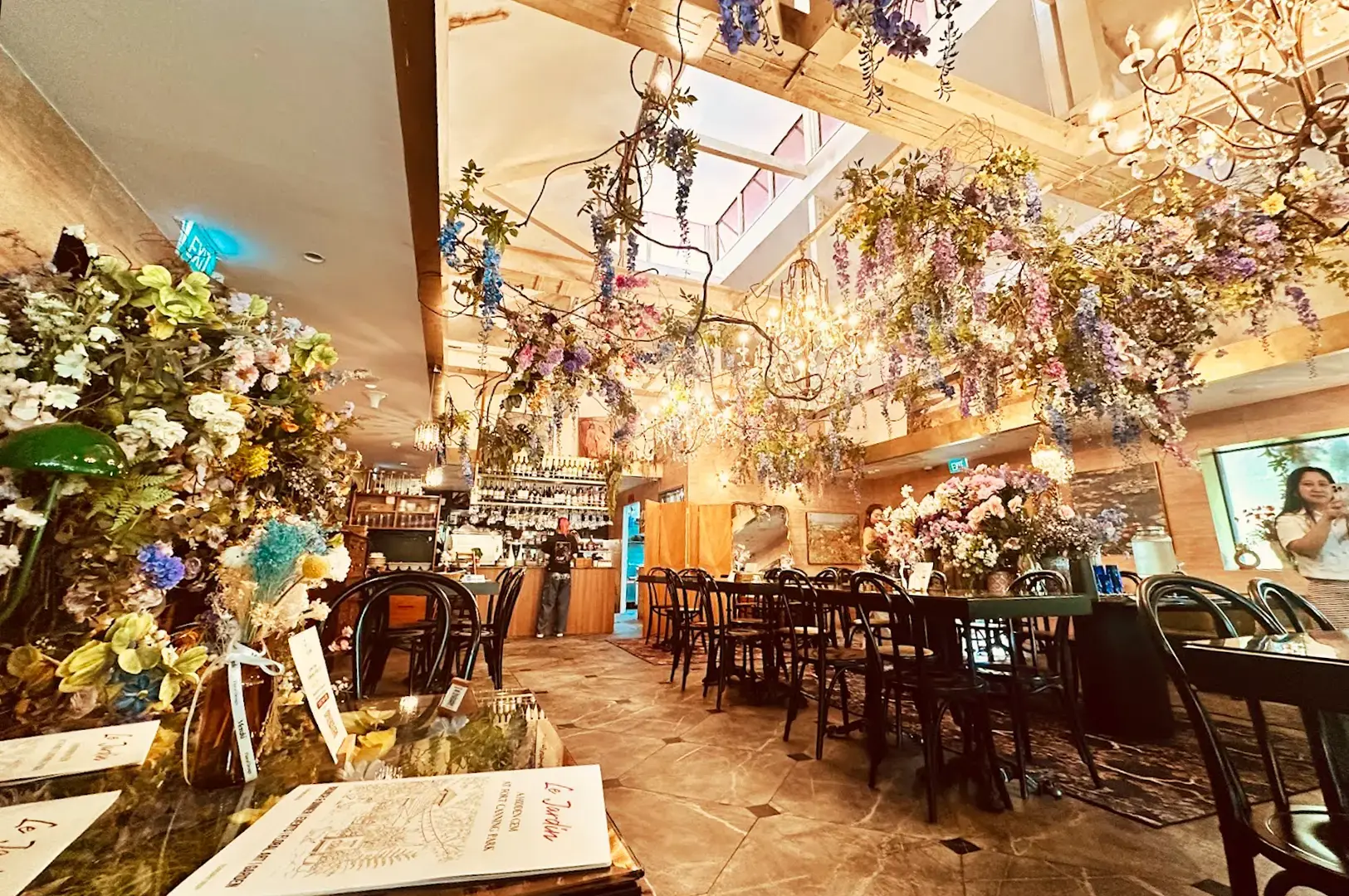 Spacious dining area at Le Jardin, Singapore, highlighting the restaurant’s signature aesthetic with cascading floral decorations, high ceilings, and a charming botanical atmosphere.