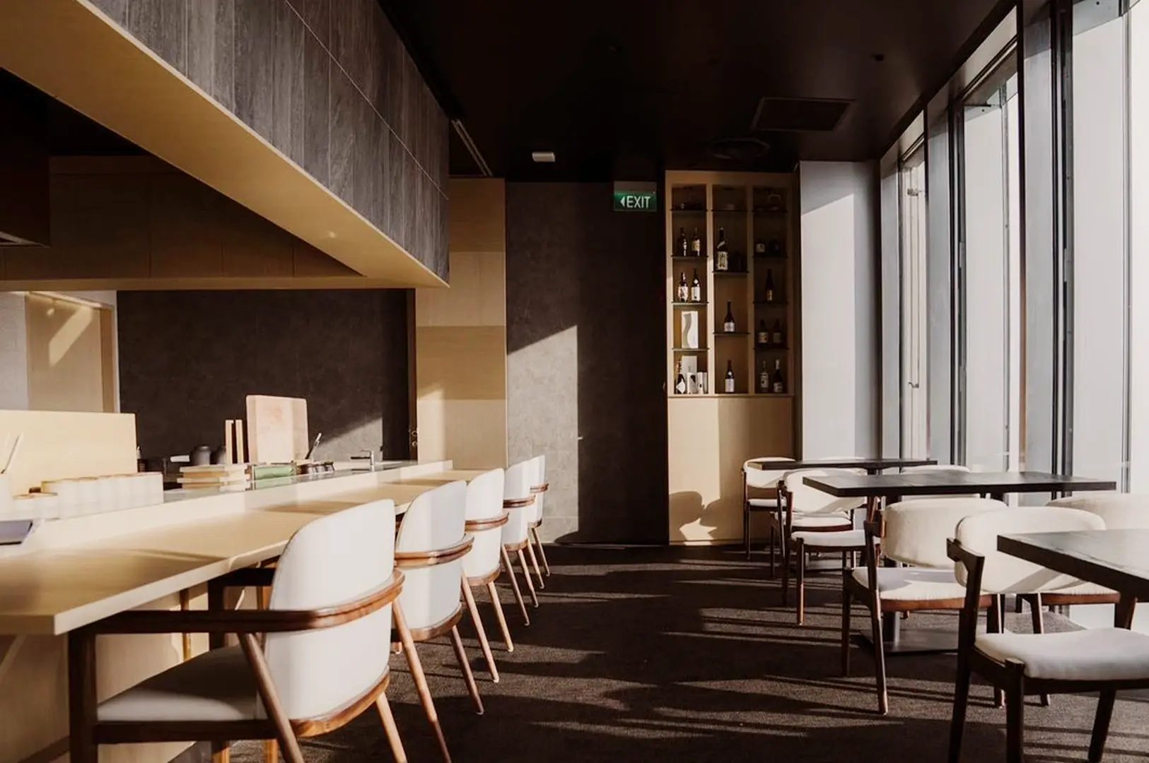 Bright and modern dining area at OUMI restaurant featuring a clean minimalist aesthetic, wooden accents, and a curated Japanese sake display.