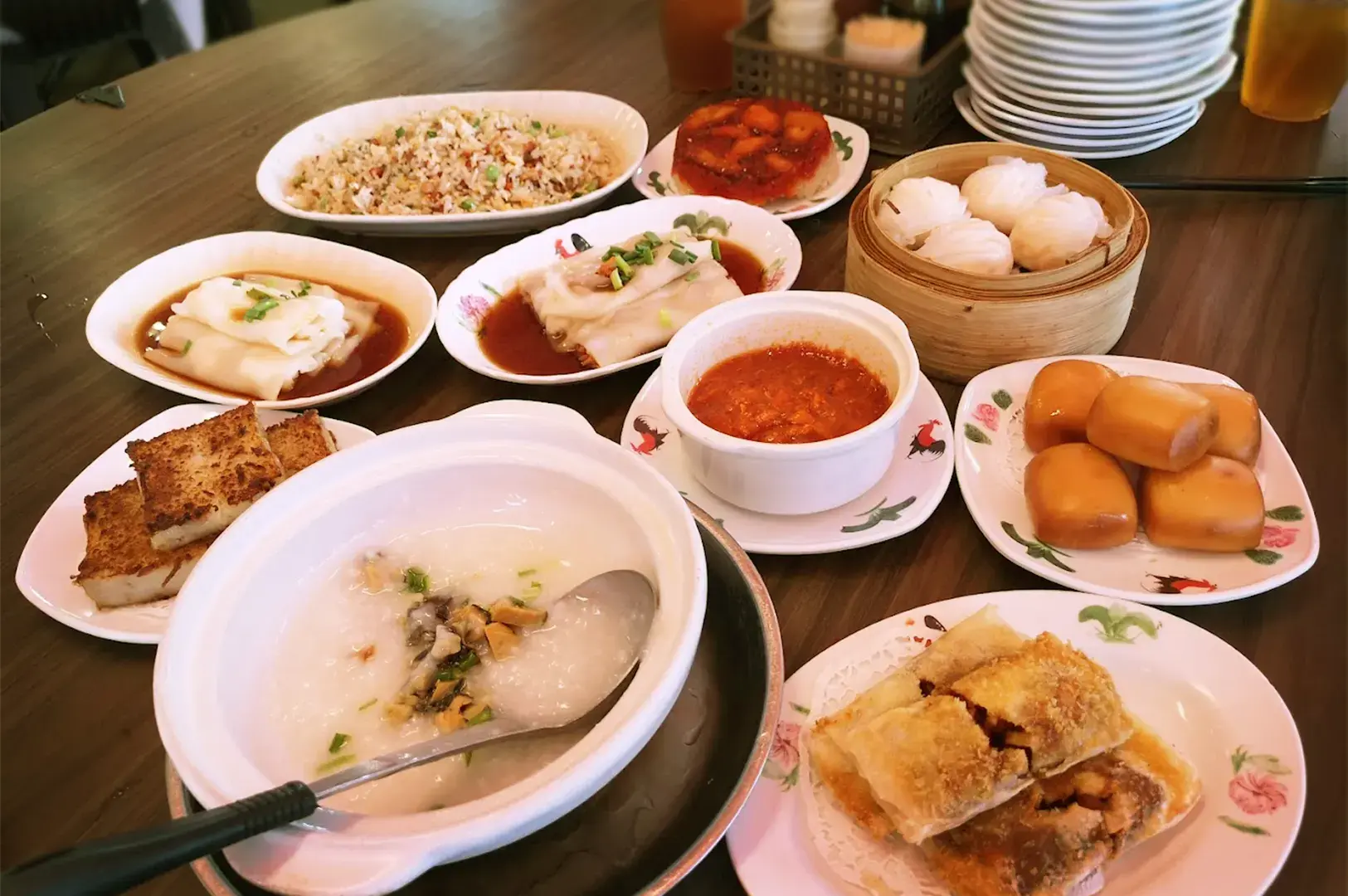 A diverse spread of traditional dim sum favorites, including steamed rice rolls, buns, and congee, arranged on a restaurant table reflecting the rich variety of local food in Geylang.