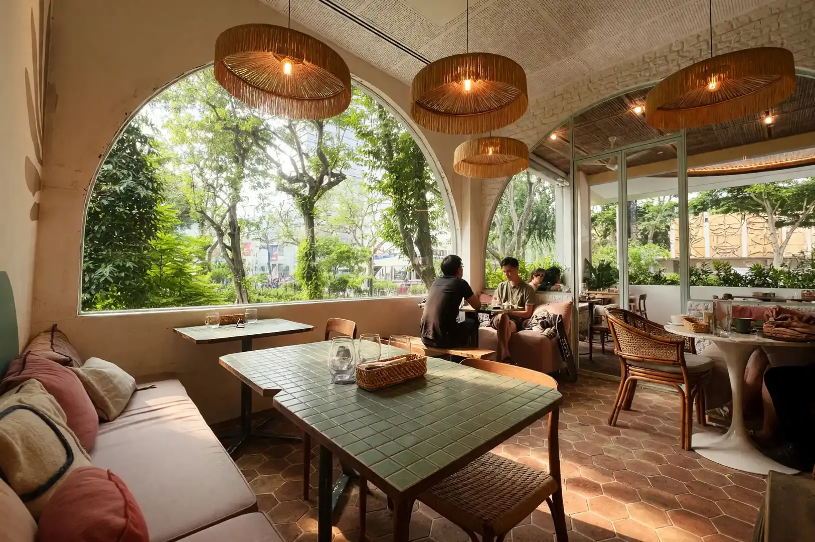 Cozy cafe seating area at Merci Marcel, Palais Renaissance, with large arched windows offering a view of lush greenery, perfect for a peaceful and aesthetic French brunch.
