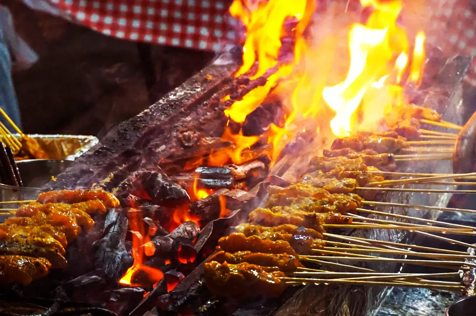 Close-up of traditional meat satay skewers grilling over glowing charcoal flames at Lau Pa Sat, highlighting the authentic Singaporean cooking method and the rich, charred texture of the food.