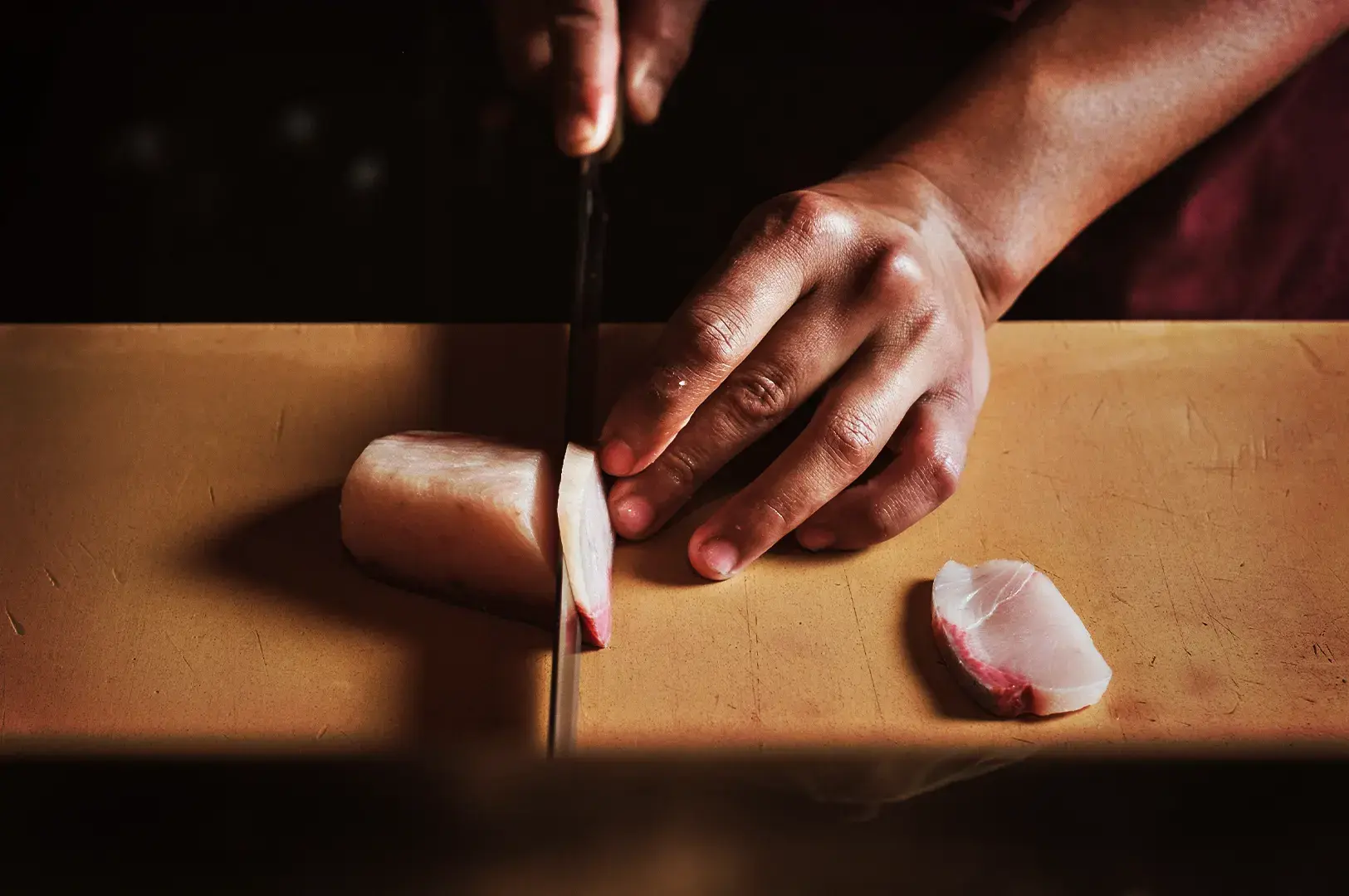 A chef's hands expertly slicing fresh sashimi with a sharp knife on a wooden cutting board, highlighting the artistry of lunch omakase.