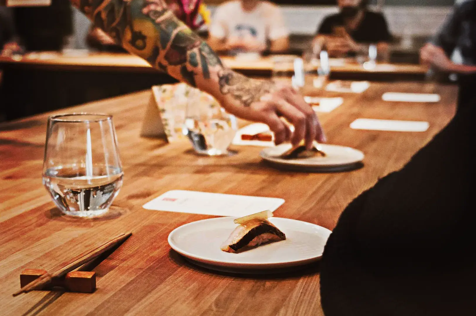 A chef serving a piece of sushi to a customer at a wooden counter during an exclusive lunch omakase experience.