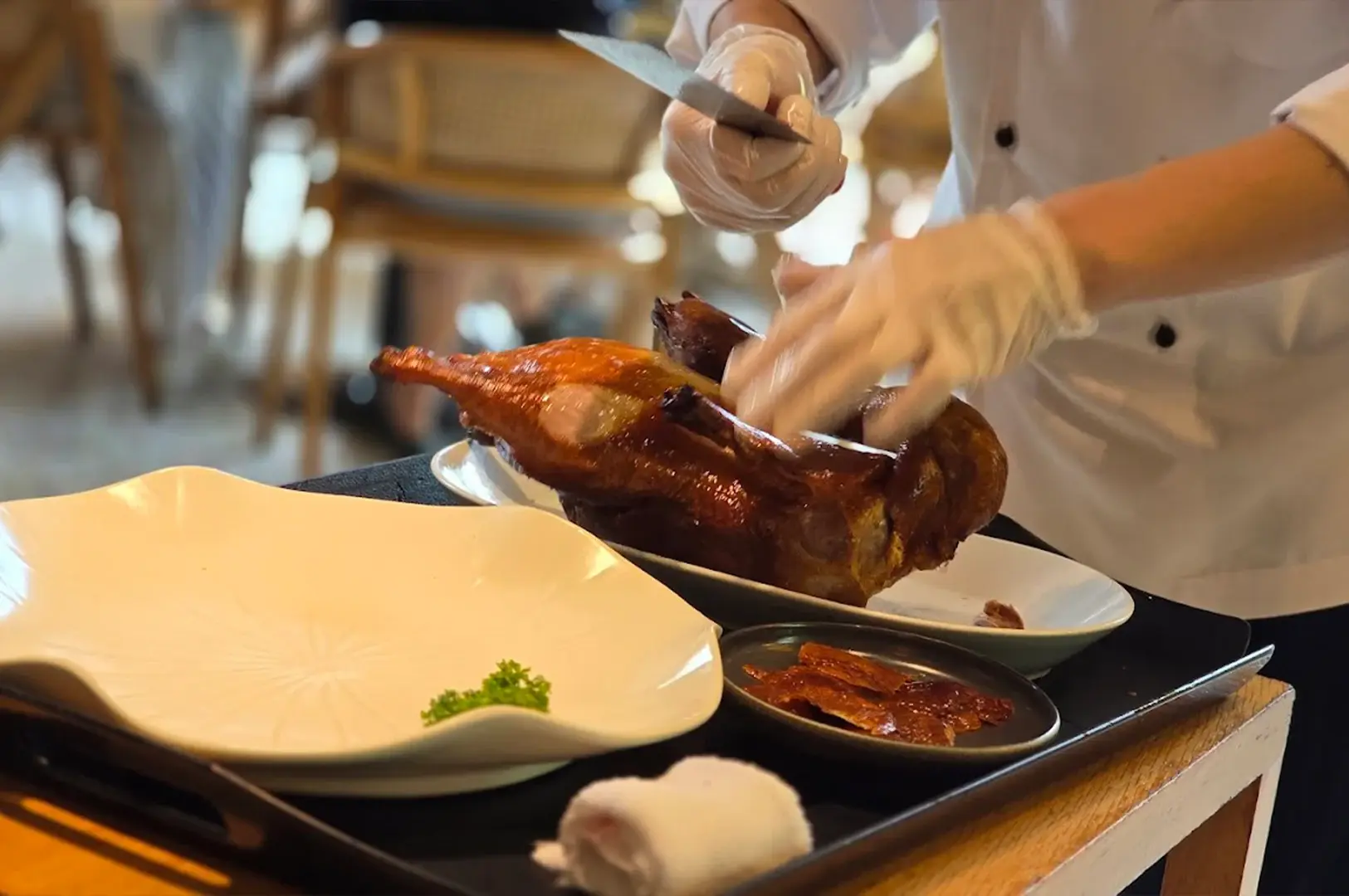 A professional chef expertly carving signature Peking duck tableside at Min Jiang at Dempsey, highlighting the restaurant's commitment to authentic culinary craftsmanship.
