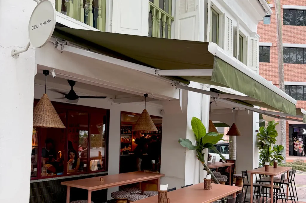 The heritage exterior of Belimbing Singapore restaurant, featuring classic colonial architecture, a green awning, and inviting outdoor terrace seating.