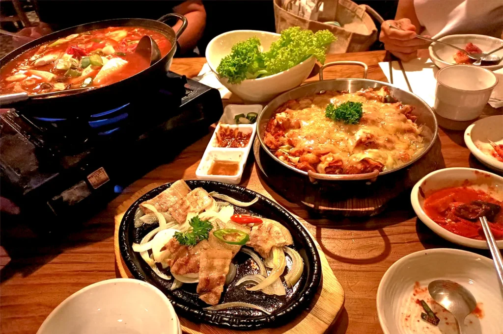 A spread of authentic Korean dishes at Todamgol in Tanjong Pagar, featuring a bubbling spicy stew, cheesy dak galbi, and grilled pork belly on a hot plate, perfect for a celebratory dinner.