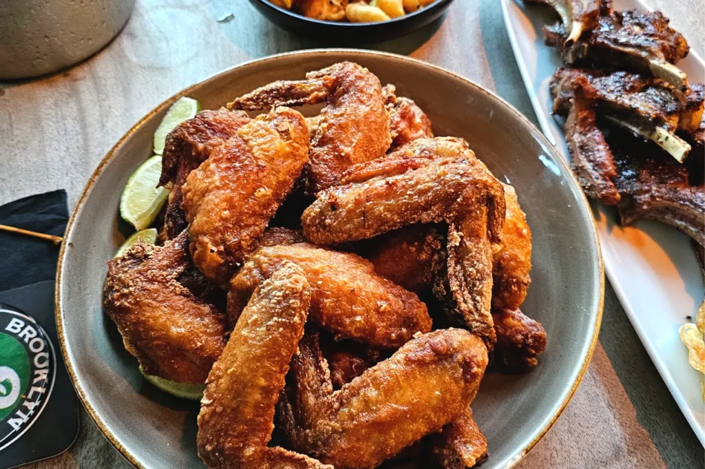 A vibrant plate of crispy fried chicken wings garnished with lime wedges, served as part of a shared meal during a rainy day in Singapore, representing the comfort of familiar flavors and conversation.