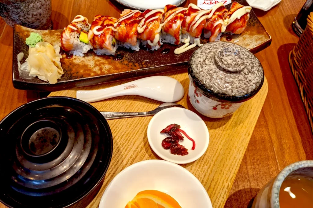 An elegantly presented Japanese set meal at Kuro Maguro, Tanjong Pagar, featuring a seared sushi roll, pickled side dishes, and traditional tea, inviting a moment of quiet, mindful observation.