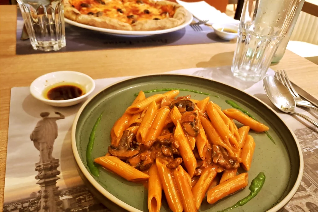 A plate of mushroom penne pasta served and a classic Italian pizza at a restaurant on Keong Saik Road, Singapore, capturing the blend of Italian culinary traditions, memory, and migration within the local dining culture.