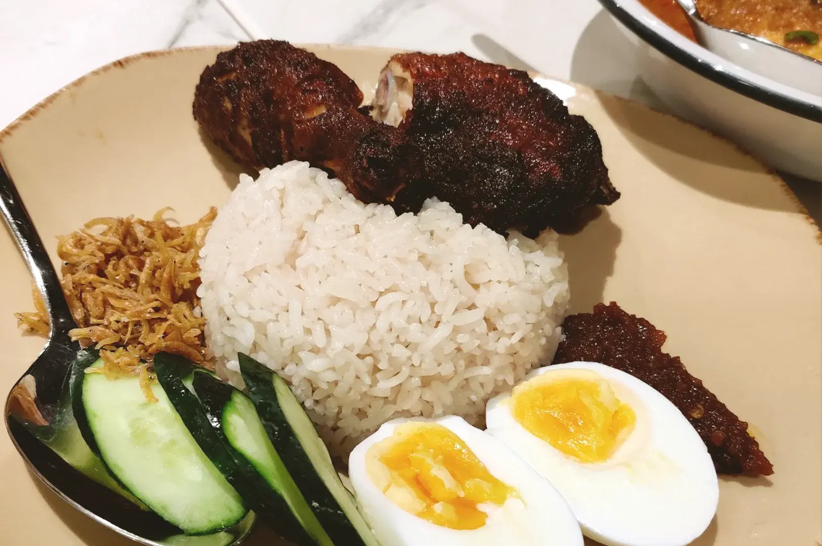 A beautifully plated serving of Nasi Lemak at Rempapa, featuring crispy fried chicken, aromatic rice, sambal, and fresh cucumber, highlighting the restaurant's focus on authentic heritage cuisine.