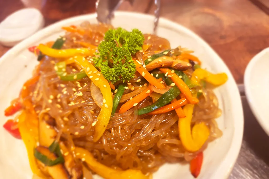 A close-up view of Japchae, a traditional Korean glass noodle stir-fry with colorful vegetables and sesame seeds, served at the popular Tanjong Pagar restaurant, Todamgol.