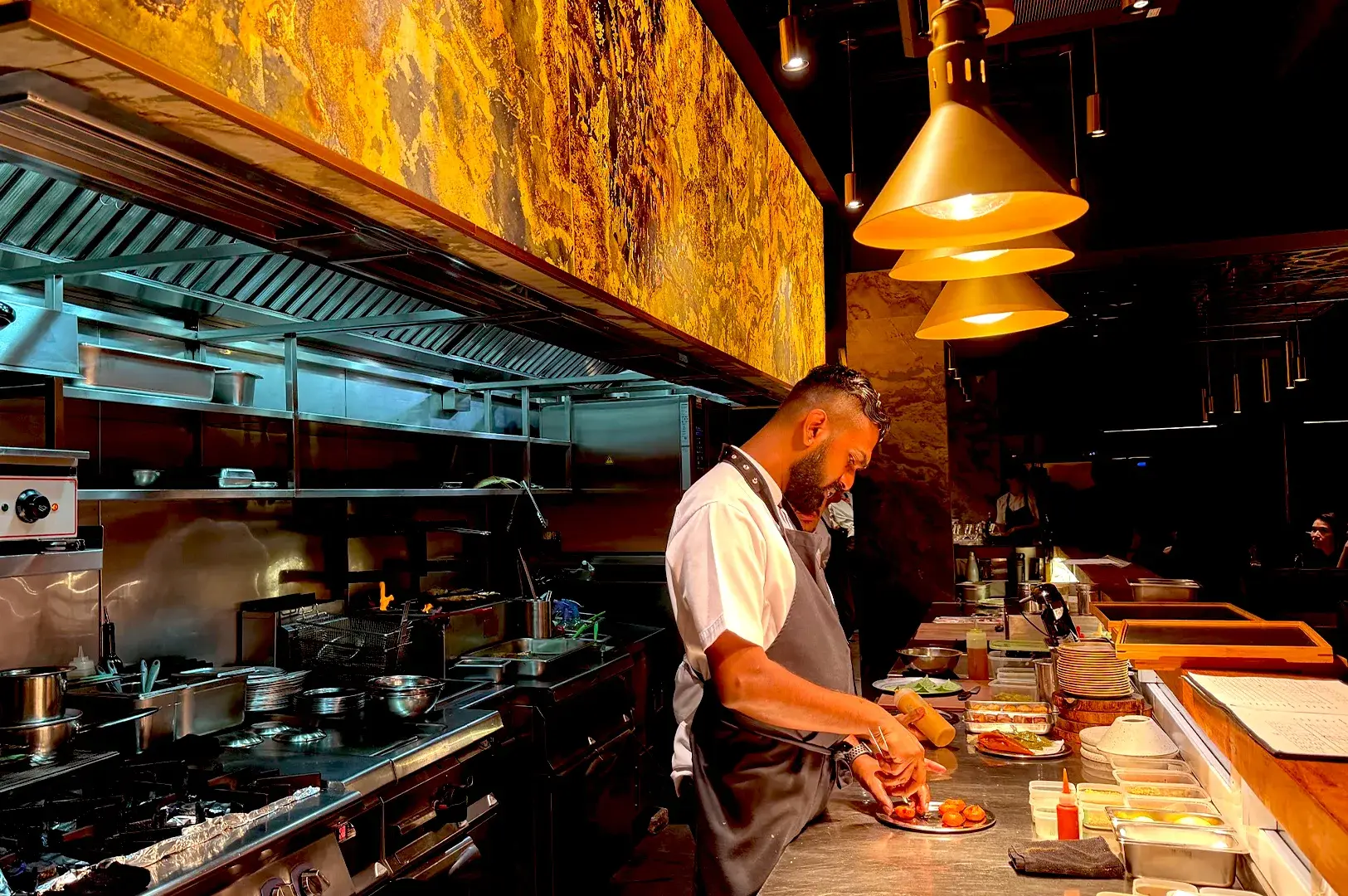 Chef Mano Thevar working in the open kitchen of his refined Singapore restaurant, demonstrating the meticulous craftsmanship behind his innovative, modern Indian dishes.
