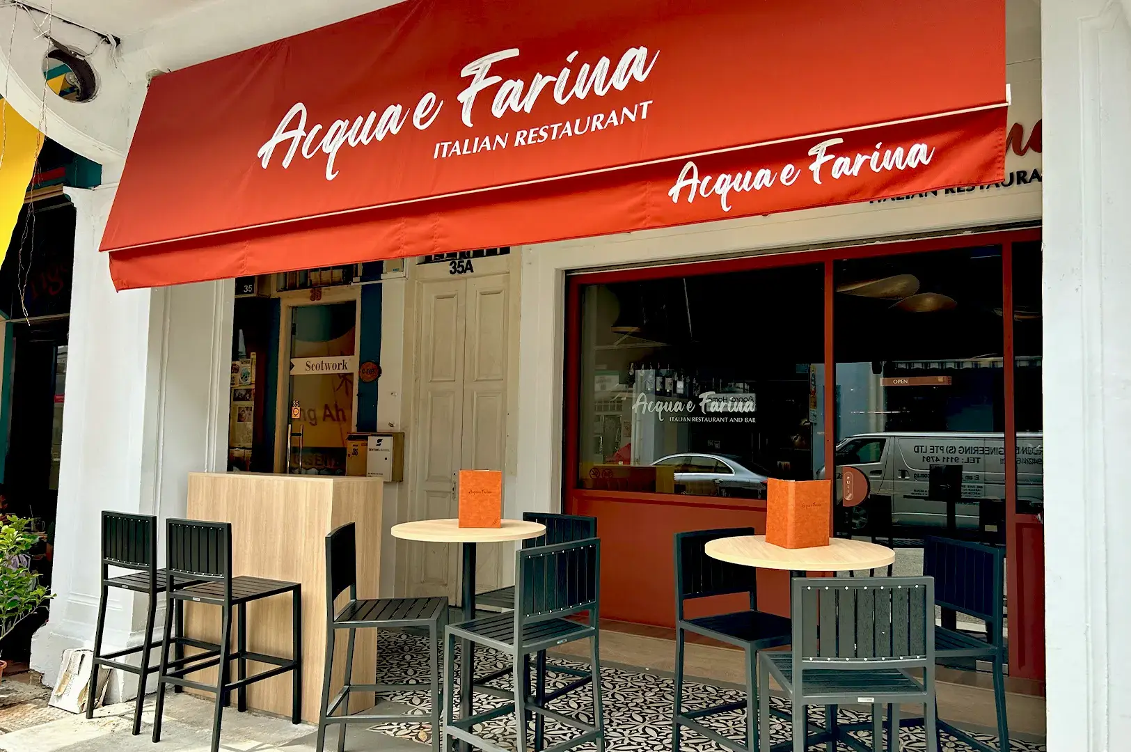 The inviting storefront of Acqua e Farina, an authentic Italian restaurant in Singapore, featuring outdoor seating and a signature red awning.