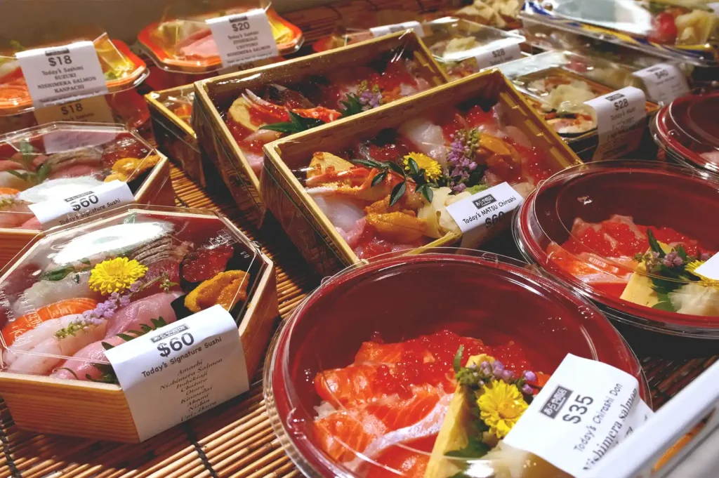 Close-up, high-angle interior shot of a refrigerated display case at Araya Shouten showcasing an array of fresh, premium Japanese sashimi boxes and chirashi dons after dark, featuring glossy salmon roe, rich uni, and neatly priced bento sets on bamboo mats.