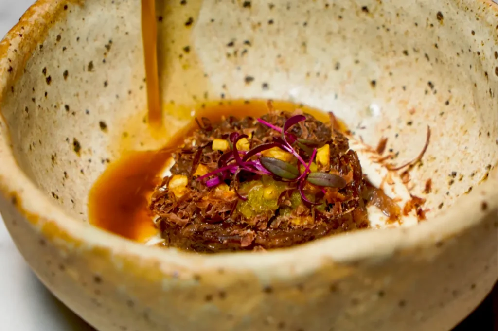 Close-up of rich, savory beef broth being poured over angus oxtail, emphasizing the attention to detail at Belimbing restaurant.