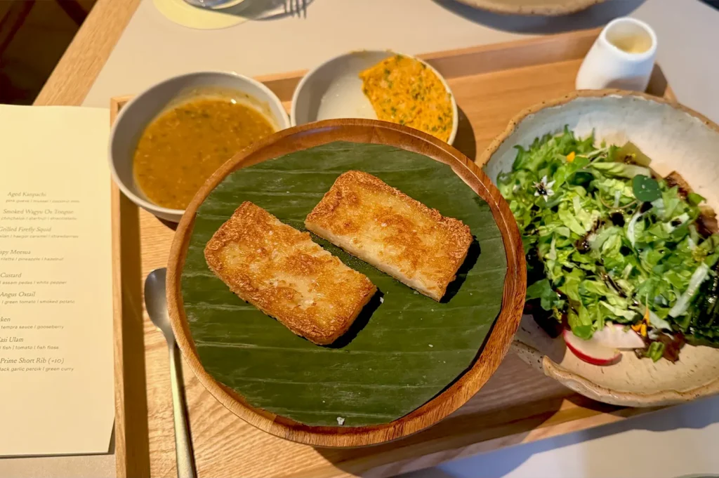 A beautifully arranged Singaporean set meal featuring crispy meesua, fresh salad, and side dishes served on a wooden tray at Belimbing.