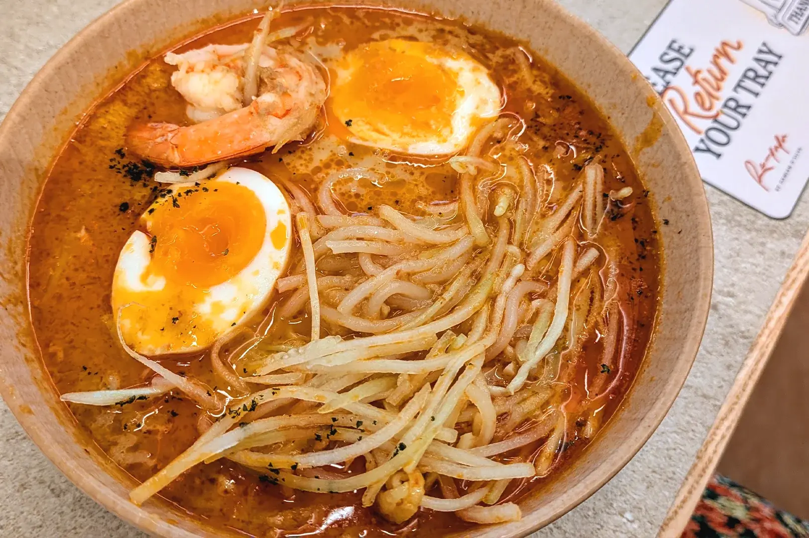 A close-up of a classic Peranakan Laksa, topped with a soft boiled egg, reflecting the traditional cuisine that is served in Rempapa.