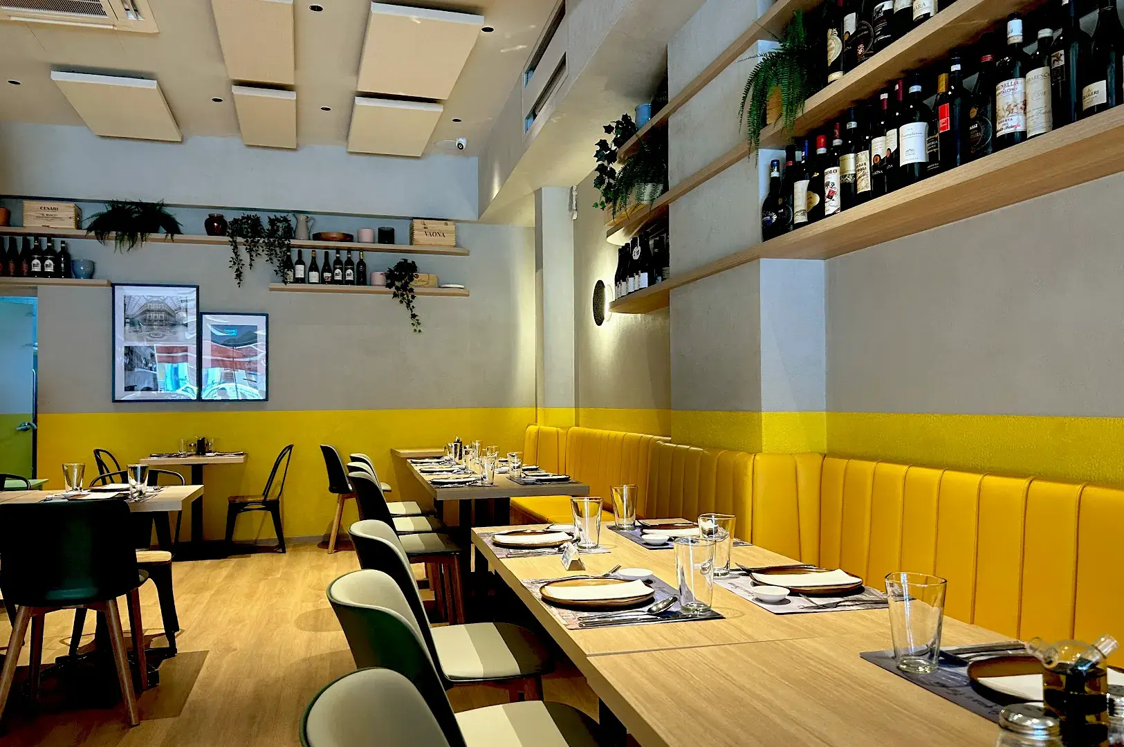 The cozy, modern interior of Acqua e Farina, showcasing warm yellow banquet seating, wooden tables, and curated Italian wine displays.