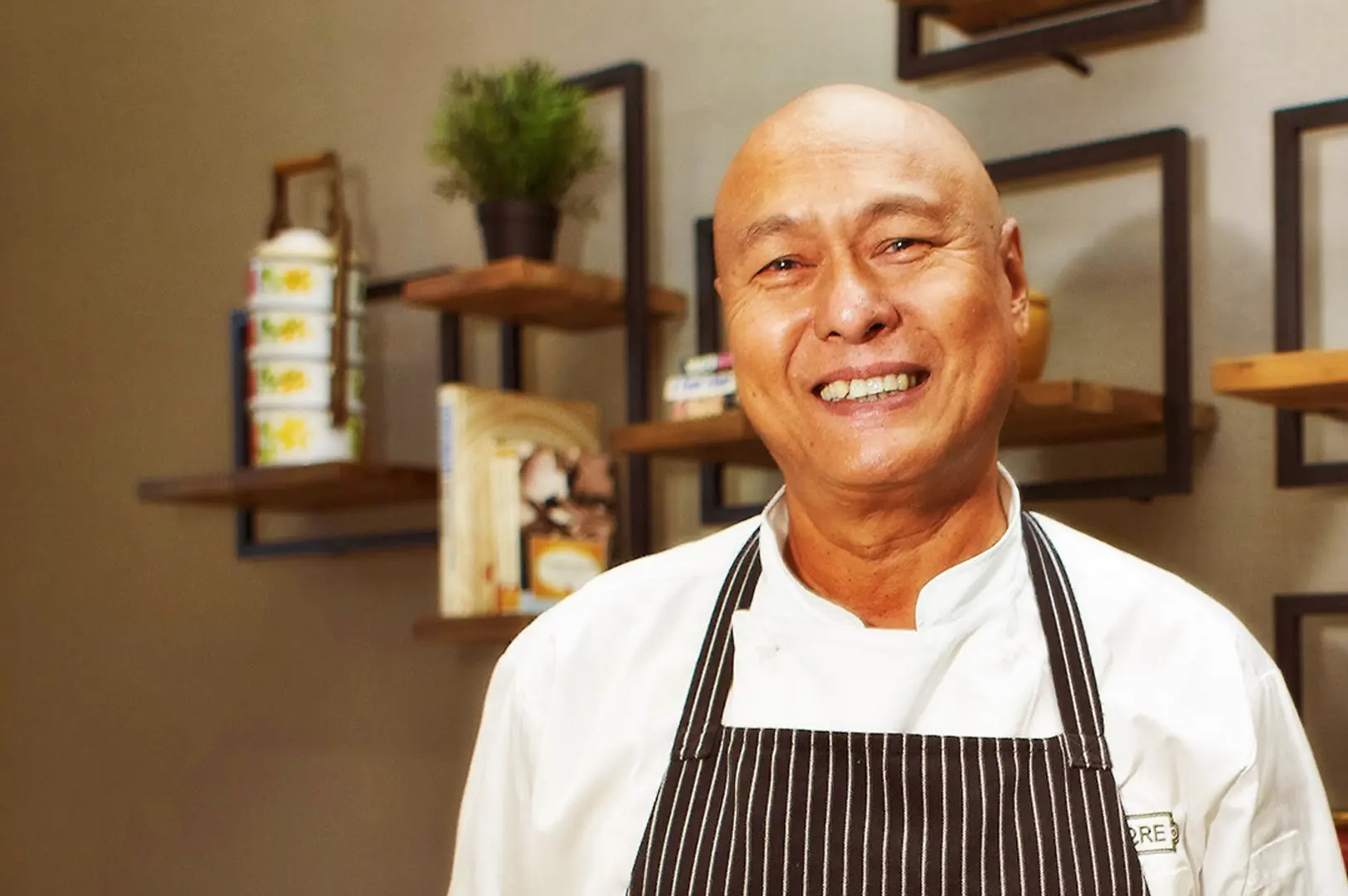 Portrait of Chef Damian D'Silva smiling in his chef's uniform at Rempapa, highlighting his role as a master of Singaporean heritage cuisine.