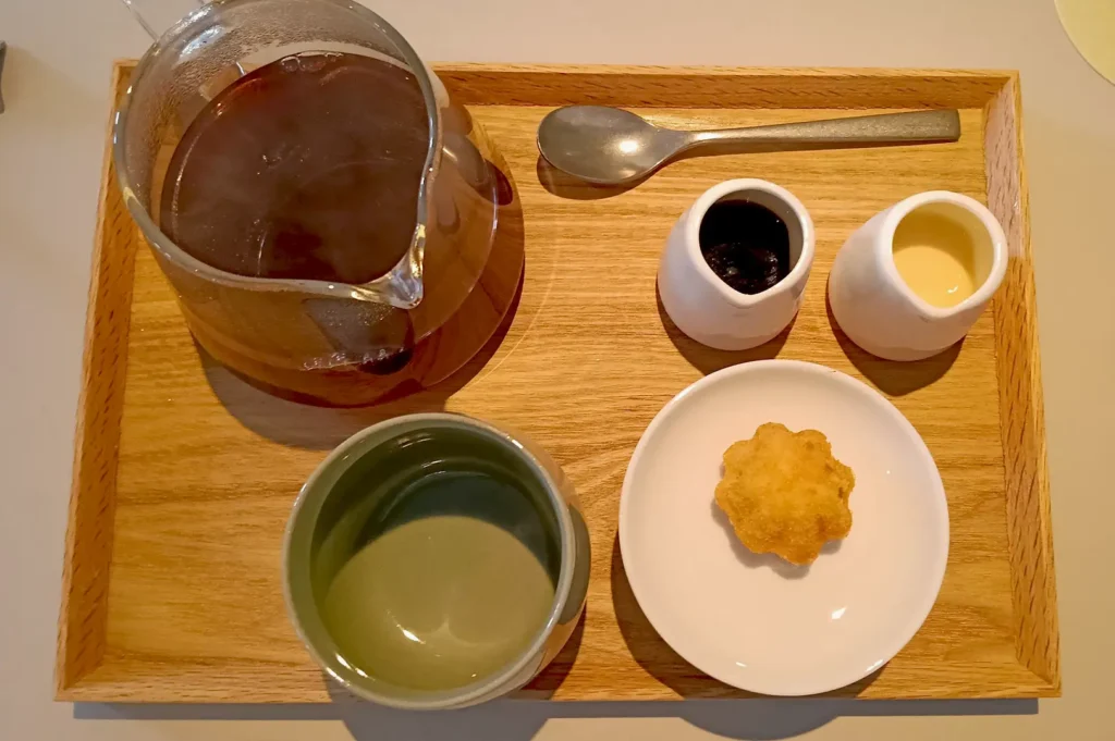A minimalist, artisanal corn tea service set with a glass teapot and ceramic cup, typical of the curated dining experience at Belimbing.