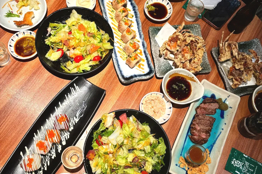 A vibrant table spread of diverse sushi platters, fresh salads, and grilled dishes at Sushi Tei, illustrating the restaurant's extensive and crowd-pleasing Japanese menu.