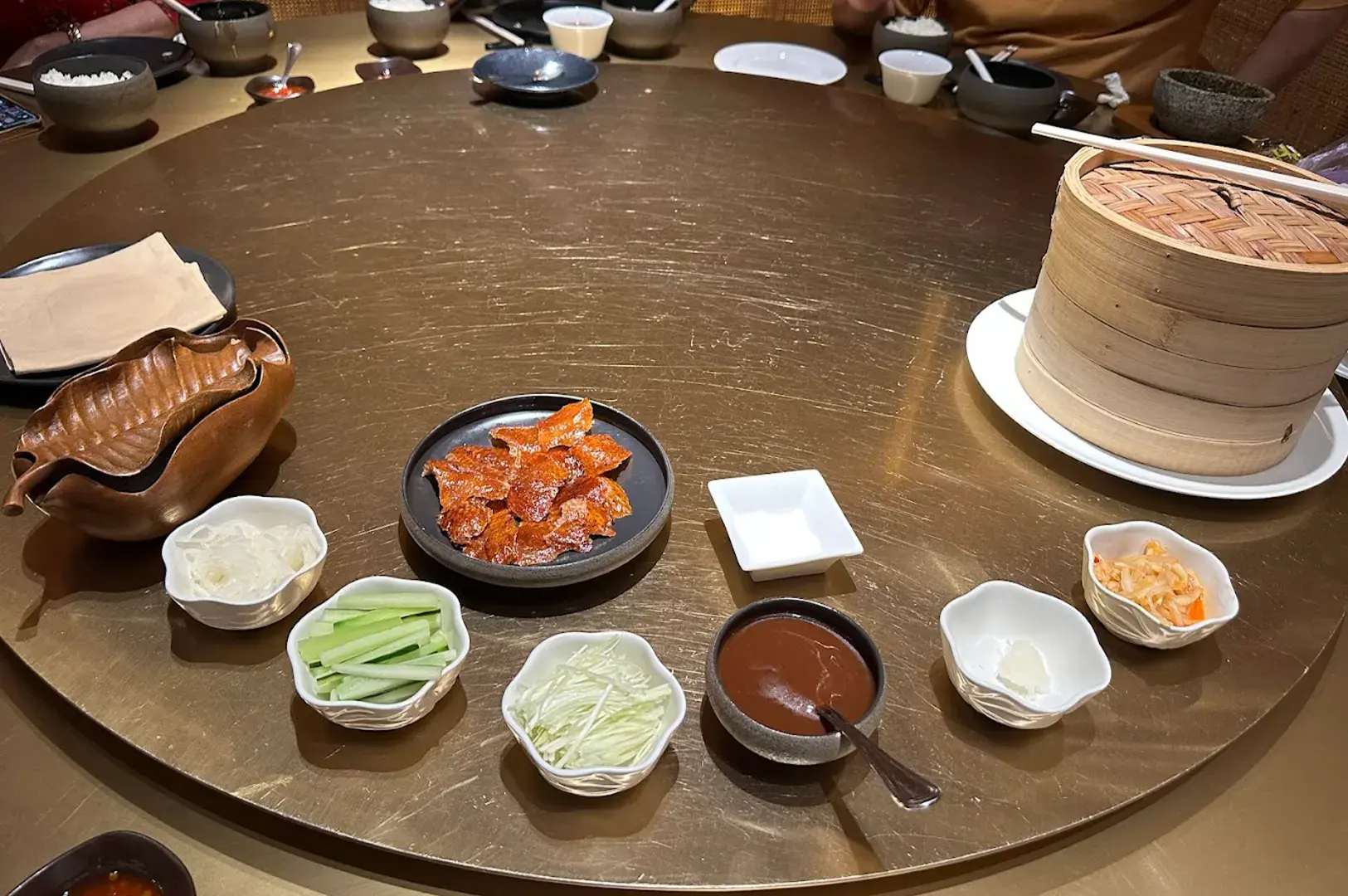 A traditional round table setting at Min Jiang at Dempsey, showcasing a premium Peking duck spread with crispy skin, cucumber, scallions, and signature sauces ready for service.