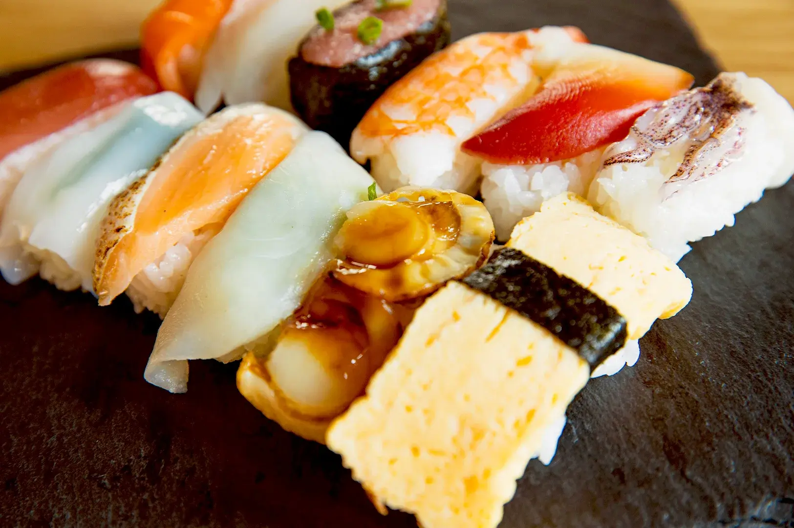 A high-quality assortment of various nigiri sushi, including salmon, scallop, and tamago, displayed on a stone slate, representing the shift toward elevated sushi craftsmanship in Singapore.