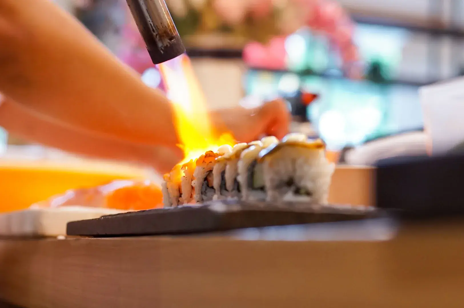 A chef using a blowtorch to sear a sushi roll, highlighting the modern culinary techniques used in omakase Japanese dining in Singapore.