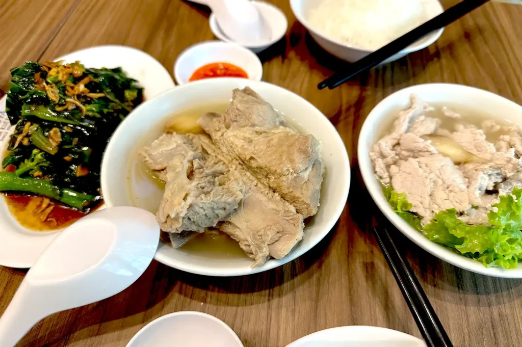 A traditional Singaporean meal of Bak Kut Teh, featuring pork ribs in herbal broth, sliced pork soup, stir-fried greens, and rice, capturing the authentic, unopposed nature of local hawker soul food.