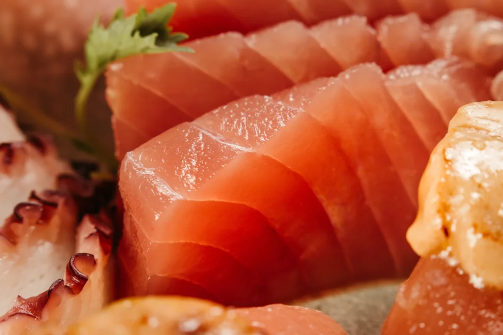 A close-up, high-quality shot of fresh, thick-cut tuna sashimi and other Japanese seafood delicacies, highlighting the textures of the best sashimi available in Singapore.