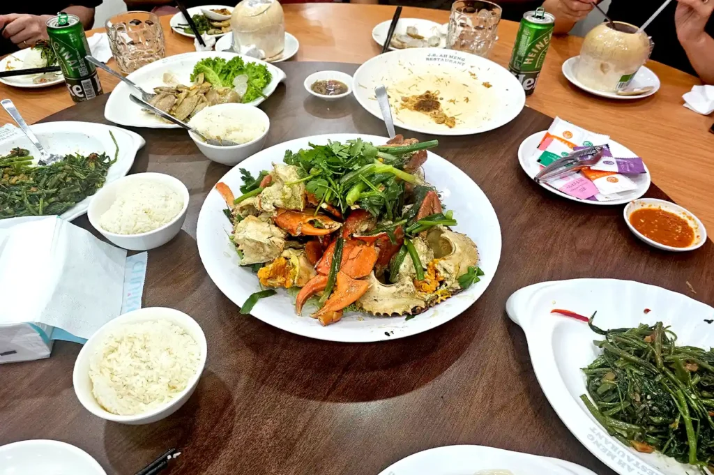 A shared table of communal Chinese dishes, including crab and stir-fried vegetables, symbolizing how social dining habits and priorities evolve with friendships as we grow older.