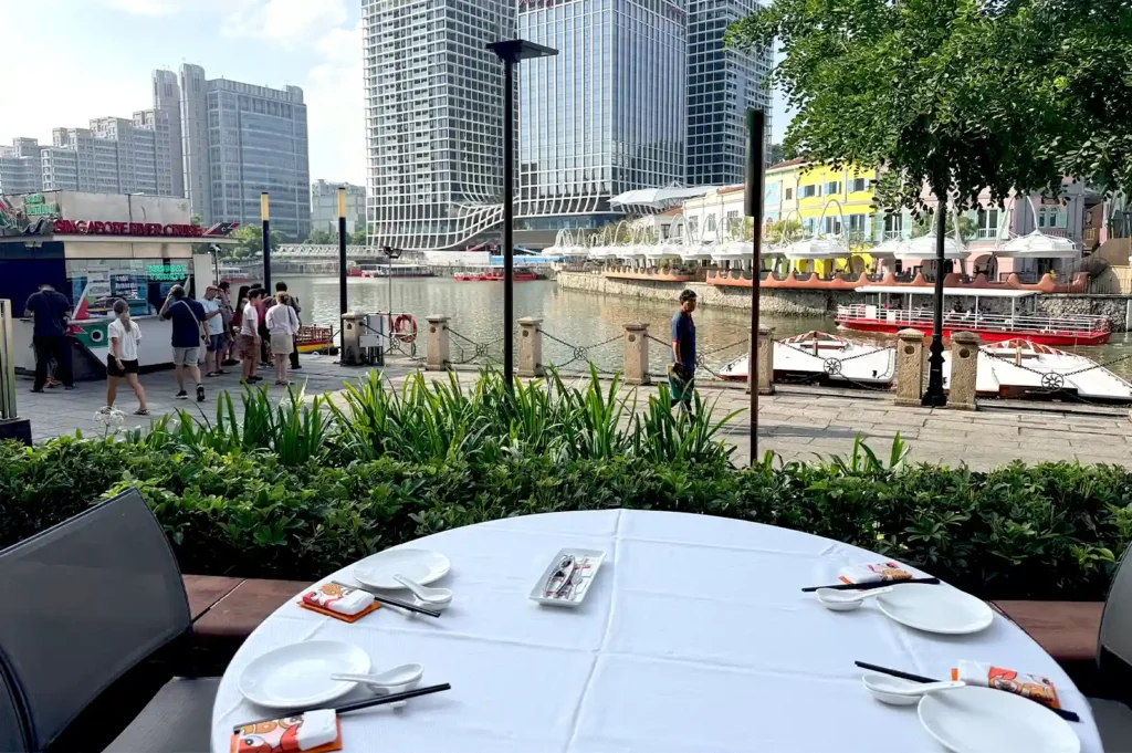 A scenic outdoor restaurant dining table with a white tablecloth overlooking a river and modern city skyline, highlighting generational differences in valuing restaurant atmosphere.