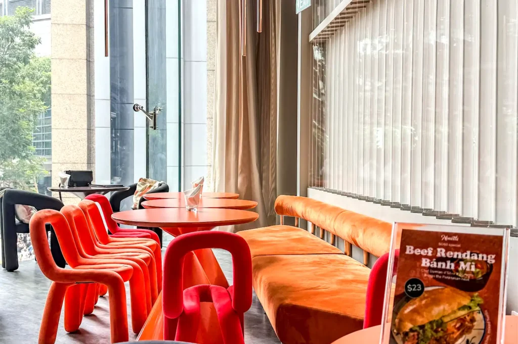 Bright, modern dining interior featuring orange chairs and banquette seating next to floor-to-ceiling windows at Rasa Space in Republic Plaza.