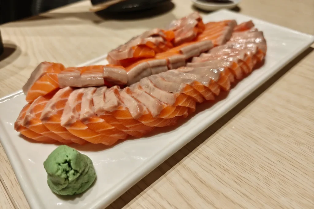Freshly sliced thick salmon sashimi served on a long white plate with a side of wasabi, highlighting the quality of sashimi available at top Singapore sushi restaurants.