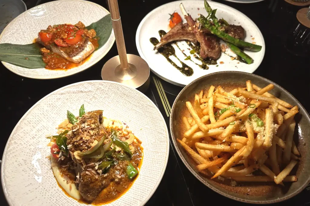 A spread of gourmet dishes including fine-dining plates, grilled meat with asparagus, and truffle fries, representing the luxury experience of high-end Singapore dining.