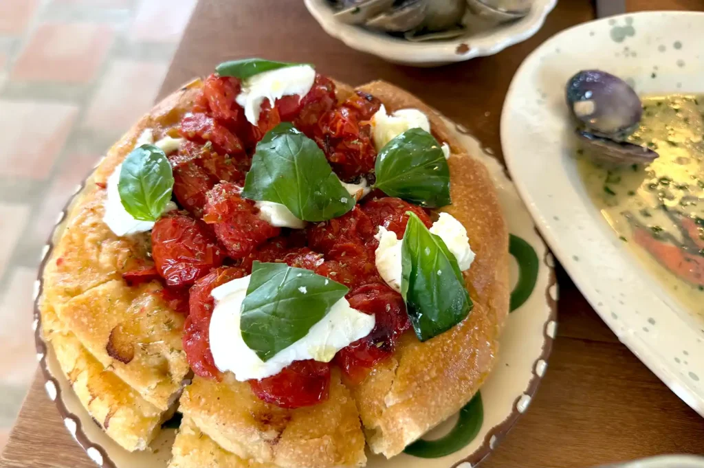 Freshly baked focaccia bread topped with cherry tomatoes, fresh mozzarella, and basil leaves served on a patterned plate at Fico Singapore.