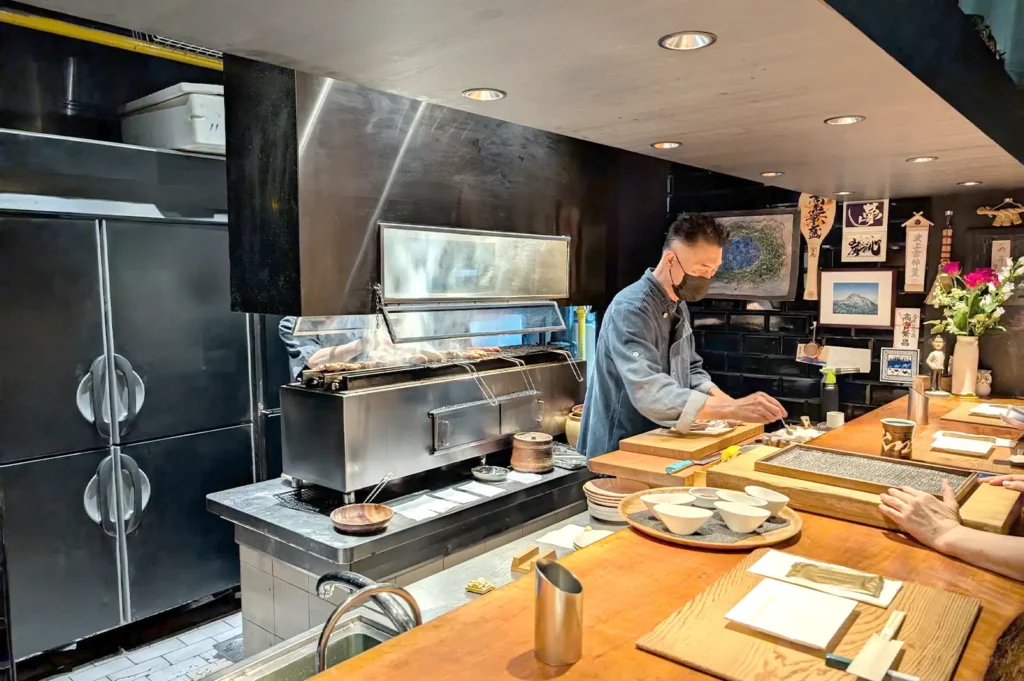 A chef at Kazu Sumiyaki Singapore working in front of an active open charcoal grill, mastering the art of Japanese sumiyaki and yakitori grilling.