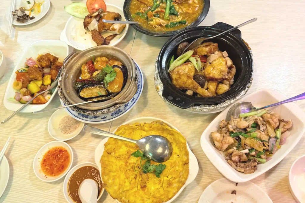 A generous spread of traditional zi char dishes—including claypot meals, fried egg, and stir-fried meats—laid out on a restaurant table, highlighting the communal joy of food culture in Singapore.