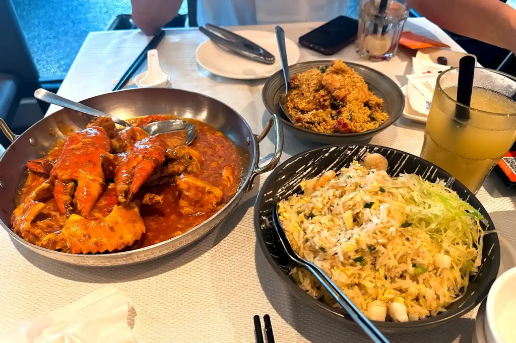 A hearty spread of traditional local dishes including chili crab, fried rice, and seafood, illustrating how older and younger diners approach food and dining value differently.