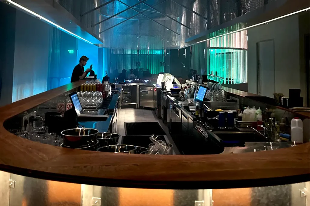 A sleek, curved wooden bar counter with ambient blue and green backlighting inside Rasa Space at Republic Plaza.