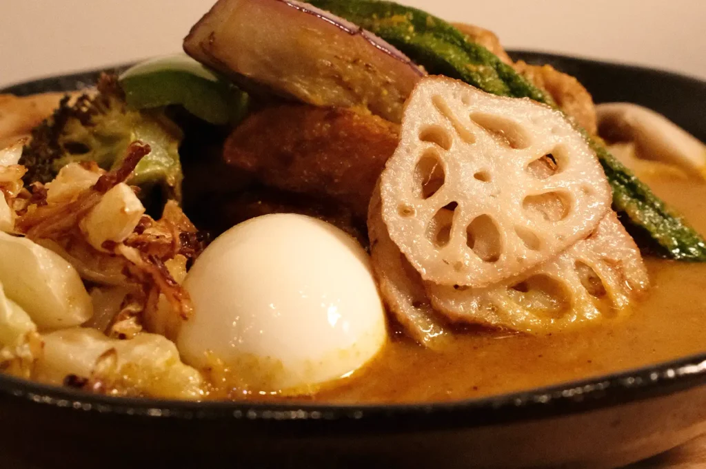 A close-up view of Soup Curry by Ki-setsu featuring signature toppings like lotus root, eggplant, okra, and a soft-boiled egg in a flavorful broth.
