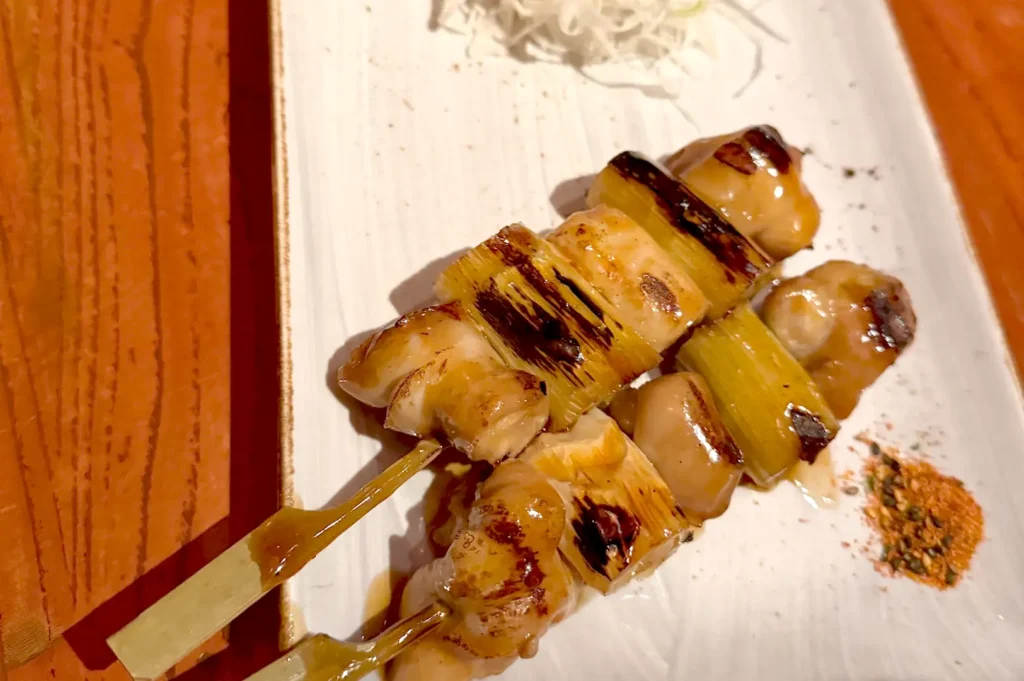 Grilled chicken skewers (yakitori) with leeks and a side of shredded cabbage served on a white plate, showcasing the culinary detail and preparation behind memorable dishes.