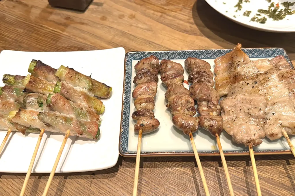 A close-up of beautifully charred Japanese yakitori skewers and grilled meat platters from Kazu Sumiyaki Singapore, showcasing expert charcoal grilling.