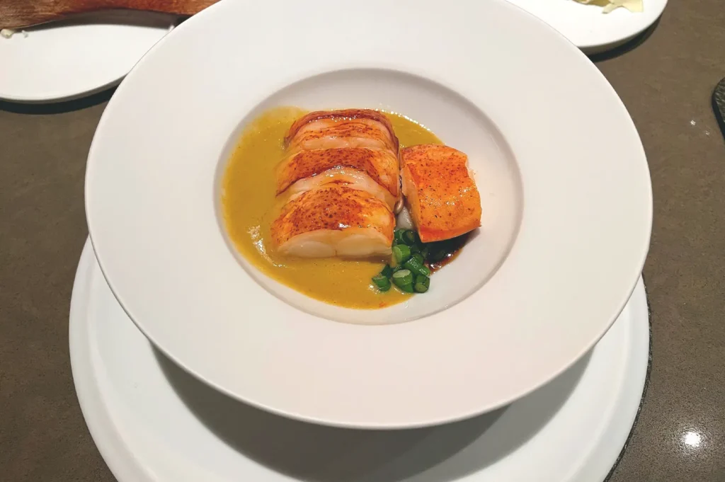 Mangrove wood charred blue lobster with laksa leaf sauce served in a white bowl at Seroja in Singapore.