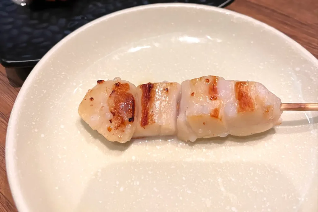 "A single chicken sashimi skewer with a perfect smoky char on a white ceramic plate at Kazu Sumiyaki Singapore.