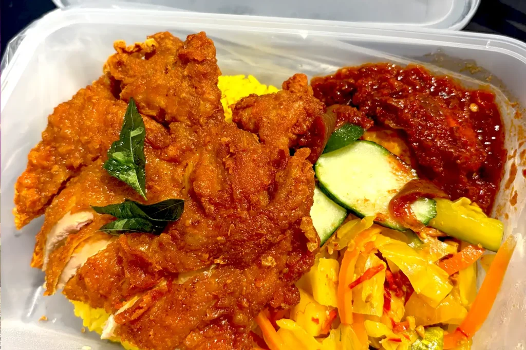 A takeaway container featuring Green Chili's aromatic ayam goreng berempah with vibrant turmeric rice.