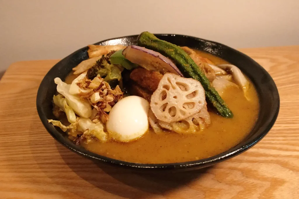 A freshly prepared bowl of Soup Curry by Ki-setsu served on a wooden table, emphasizing the lighter, soup-like consistency compared to thick Japanese curry.